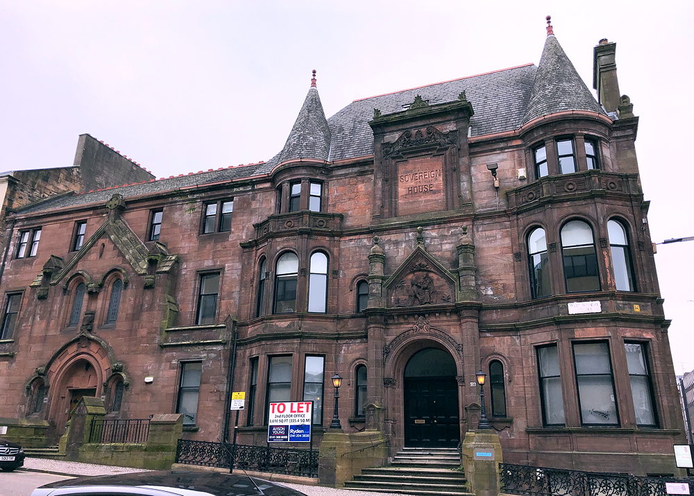 A large Victorian building built of red sandstone with two pepper-pot turrets and a large carving above the main door.
